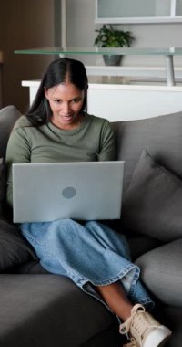 Dikey video: Laptopta mesaj keşfetmek, Hintli bir çiftin kanepede sohbet etmesi ve kupaları paylaşması. Samimiyet, samimiyet, modernlik, iletişim, bağlantı, rahatlama, dikey video