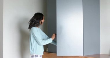 Askıları tutan, giysi seçen kadın gardırop çubukları ve ışık düğmesi olan bir kadın. Kostüm, moda, organizasyon, minimalizm, yaşam tarzı, iç mekan, iç mekan