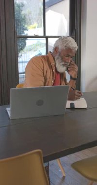 Dikey video: Çağrı sırasında Afro-Amerikalı adam not alıyor ve evdeki bilgisayarları kontrol ediyor. Profesyonel, çalışma alanı, modern, odaklanma, konsantrasyon, üretkenlik, dikey video