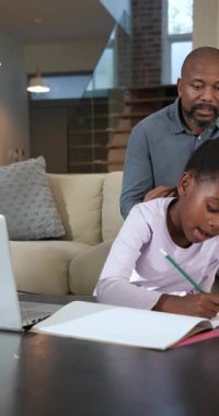 Dikey video: Bir baba durakladıktan sonra deftere işaret ederek kızına yazı yazmasında yardım ediyor. Aile, danışmanlık, eğitim, bağlanma, atölye, işbirliği, dikey video