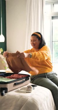 Dikey video: Yetişkin bir kadın telefonu kontrol ediyor sonra seyahat için bavulunu yatak odasına yerleştiriyor, fotokopi odası. Seyahat, paketleme, organizasyon, yaşam tarzı, konforlu, hazırlık, dikey video