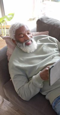 Dikey video: Yaşlı Afro-Amerikan bir adamın dinlenmek için tablet çalmasından sonra. Son sınıf, rahatlama, teknoloji, rahatlık, konfor, yaşam tarzı, dikey video