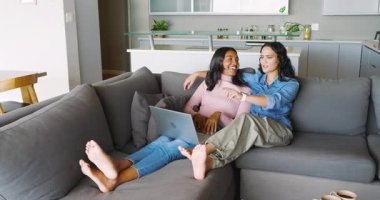 Farklı kadın partnerler evdeki bölmeli koltukta yastıklarla dizüstü bilgisayarlarını paylaşıyorlar. Samimiyet, dostluk, rahatlama, çağdaş, yaşam tarzı, dijital, konfor