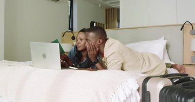 Misafir odasına giren, pasaport çıkaran, dizüstü bilgisayarda rezervasyon formlarını dolduran Afro-Amerikan çift. Seyahat planlama, romantik çift, dijital göçebeler, işbirliği, modern dekor, samimiyet, teknoloji