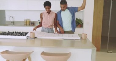 Mutfak adasının üzerine eğilmiş, boyutları belirten ve fikirleri tartışan bir çift. Mimari, işbirliği, modern, tasarım, planlama, iç mimari, ortaklık