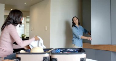 Bayan arkadaşlar yatak odasına açık bavul hazırlıyorlar. Hasır şapkalı, ahşap askılı. Bavul, seyahat, organizasyon, yaşam tarzı, minimalist, sıcak tonlu, arkadaşlık