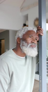 Dikey video: Son sınıf öğrencisi kapı çerçevesine yaslanıyor açık hava ışığını ölçüyor ve eve gülümsüyor. Düşünce, dinginlik, modern, iç mekan, mimari, son sınıf, dikey video