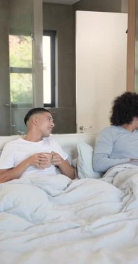 Kıvırcık saçlı adam elinde seramik bardakla içeri giriyor, kahve eşine uzatıyor ve yatağa sarılıyor. Romantizm, samimiyet, rahatlama, şefkat, rahatlık, dikey video