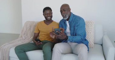 Evdeki kanepede akıllı telefonları değiş tokuş ederken beni Afrikalı Amerikalı baba ve oğul olarak görmek. Aile, bağ, teknoloji, iletişim, modern, samimi, boş zaman