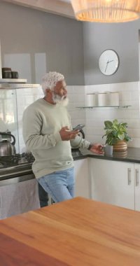 Dikey video: Mutfak araştırması, kıdemli Afro-Amerikan adam akıllı telefon kaydırma, kahve yudumlama. Modern, yaşam tarzı, günlük, rahatlama, konforlu, evcil, dikey video