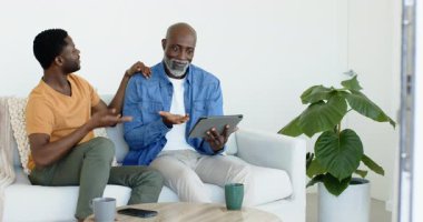 Afro-Amerikalı baba ve oğul, içeriği evde tablet sunan oğul olarak görürken kutlama yapıyorlar. Aile, akıl hocalığı, bağlanma, bağlantı, teknoloji, modern, yaşam tarzı