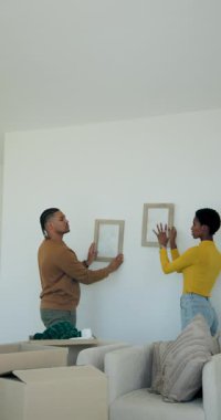 Dikey video: Eve taşınma, çeşitli çiftler oturma odasında sarılmayı planlayan çerçeveleri boşaltma. İç mekan, yenileme, mobilya, konforlu, ilişki, arkadaşlık, dikey video