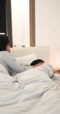 Alarm çalarken 40 'lı yaşlarda bir adam telefonda konuşuyor, 20' li yaşlarda bir adam sarılıyor, ekrana gülüyor. Morningroutine, samimiyet, bağlantı, rahatlama, şefkat, samimi, dikey video