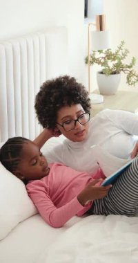 Anne ve kızı resimli kitabı yatakta açıp resimlere bakıyor ve bağlanmak için sayfaları çeviriyor. Aile, bağ, hikaye anlatma, eğitim, samimiyet, yetiştirme, dikey video