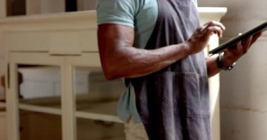 Önlük giyen kıdemli Afrikalı Amerikalı atölyede tabletle, tahta şömine rafıyla etkileşime geçiyor. Zanaatkar, yenileme, zanaatkar, sanayi, tamirci, modern, çalışma alanı