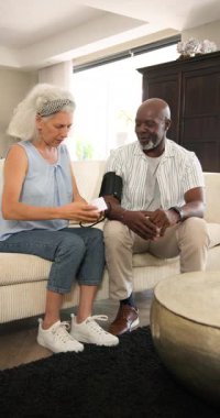 Olgun kadın monitör düğmesine basıyor yaşlı adamın koltuktaki kan basıncını ölçerken kelepçeleri şişiriyor. Sağlık, sağlık, bakım, arkadaşlık, modern, bakım, dikey video