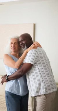 Yaşlı çift oturma odasında dans ederken erkek, kadını döndürmek ve neşeyi paylaşmak için elini kaldırır. Romantizm, arkadaşlık, zarafet, dinginlik, etkileşim, ev, dikey video