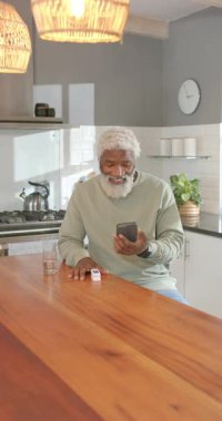 Dikey video: Mutfak adasındaki telefon alarmında glukometreyi dinleyen kıdemli Afrikalı Amerikalı adam. Teknoloji, sağlık, sağlık, modern, yaşam tarzı, dijital, dikey video