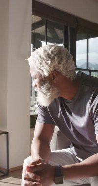 Dikey video: Evde kıdemli Afrikalı Amerikalı bir adam dağ dönüşünü fark edip gülümsüyor. Zarafet, dinginlik, kentsel lüks, yaşam tarzı, olgunluk, tefekkür, dikey video