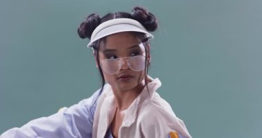 Diz çökmüş, ceketli, güneş gözlüklü ve güneşlik takan bir kadına yerleşip sette düşünceli bir poz vermek. Moda, portre, minimalizm, yaşam tarzı, eğlence, güven, tarz