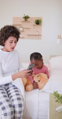 Anne, Afro-Amerikalı çocuğa yatakta ilaç veriyor sonra telefona bakıyor ve termometre kullanıyor. Bakıcı, yetiştirme, rahatlık, pediatrik, yerli, yaşam tarzı, dikey video