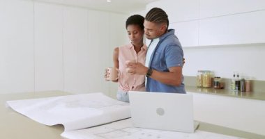 Mutfak adasına yaklaşan çift, kat planlarını açıyor ve dizüstü bilgisayarı tasarım projesi için kaydırıyor. İşbirliği, planlama, mimari, modern, birliktelik, yenilik, çalışma alanı