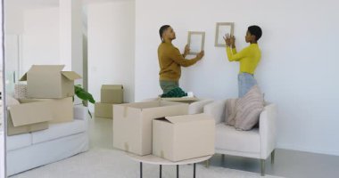 Kutulardan çerçeveleri çıkaran ve evdeki dekorasyon duvarlarını süsleyen, kucaklayan ve balkon manzarasını gösteren bir çift. Hareket, yenileme, iç mekan, uyum, bağlantı, dönüşüm, yaşam tarzı