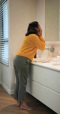 Dikey video: Kadın banyoya gidiyor, maske kesesini açmadan önce yüzünü yıkıyor. Cilt bakımı, güzellik, bencillik, minimalizm, refah, iç mekan, dikey video