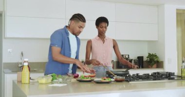 Çeşitli çiftler mutfakta yemek pişirme ipuçlarını takip ederken tavayı karıştırıyor, hamburger birleştiriyor, dans ediyor. Mutfak, takım çalışması, çağdaş, yaşam tarzı, yerli, mutlu, aktivite