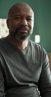 Dikey video: Yatakta kıdemli Afro-Amerikalı bir adamın gülümseyerek lense dönüşmesini gösteriyor. Rahatlama, memnuniyet, sıcaklık, sade, rahat, rahatlatıcı, dikey video