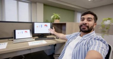 Ofis kabininde dizüstü bilgisayarları ve saksı bitkileriyle oturan Hintli adamı kaydediyor. Profesyonel, teknoloji, modern, analitik, çalışma alanı, şirket, büyüme