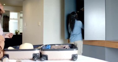 Çeşitli bayan arkadaşlar, hasır şapka ve ahşap askılarla yatak odasında bavul hazırlıyorlar. Yaşam tarzı, seyahat, paketleme, organizasyon, eğlence, çağdaş, yaşam tarzı aksesuarları