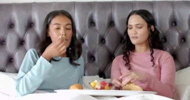 Çeşitli bayan arkadaşlar yatakta meyve kasesi ve hamur işleriyle kahvaltı tepsisini paylaşıyorlar. Samimiyet, dostluk, rahatlama, yaşam tarzı, sıcak, zarif, samimi.