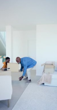 Dikey video: Afrika kökenli Amerikalı baba ve oğul oturma odasındaki kaldırma kutusundaki kutuları açıyor. Aile, ev, takım çalışması, yenileme, iç mekan, bağ, dikey video