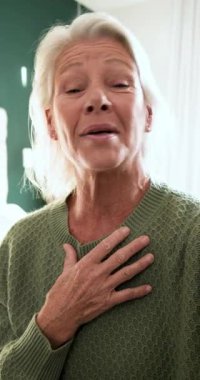 Dikey video: Yaşlı kadın elini göğsüne koyup kameraya gülüyor ve eve el sallıyor. Sıcaklık, özgünlük, ifade, iletişim, evcimen, içten, dikey video