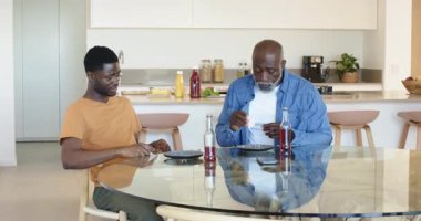 Afro-Amerikan baba ve oğlu mutfak adasındaki cam masayı yemekten sonra temizliyor. Aile, bağ, mutfak, ev, birliktelik, modern, sıradan