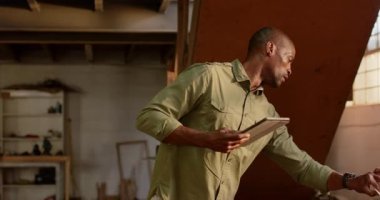 Olgun Afro-Amerikan bir adam atölyede eğiliyor ve terini pano, pencere ve fotokopi ile siliyor. Endüstriyel, işçilik, odaklanmış, çalışkan, köylü, faydacı, eğitim