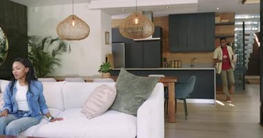 İçki getiren adam, beyaz koltukta oturan ve televizyon izleyen Afro-Amerikan çift. Yaşam tarzı, eğlence, modern, iç mekan, konfor, bağlantı, refah