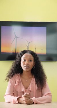 Dikey video: Rüzgâr türbini rüzgarın enerjisini açıklayan görüntü ekranından önce masasında oturan Afrikalı Amerikalı kadın. Çevre, iletişim, sunum, teknoloji, sürdürülebilirlik, modern, dikey video