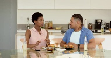 Mutfak masasındaki çeşitli çiftler hamburger kesiyor ve lezzet tasvir ediyor, adam kafa sallıyor. Romantik, yemek, destek, bağlantı, mutluluk, modern, gündelik