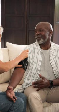 Üst düzey bir çift, kadının koluyla kanepede oturuyor ve baskıyı kontrol etmek için kelepçe takıyorlar. Bakıcı, sağlık, sağlık, arkadaşlık, dijital aygıt, konfor, dikey video