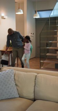 Dikey video: Afrikalı Amerikalı baba ve çocuk eve sırt çantasıyla geliyor, uzaktan kumandayı alıyorlar. Aile, bağ, modern, rahat, yaşam tarzı, etkileşim, dikey video