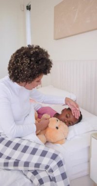 Telefon görüşmesi bitiyor, anne kızının ateşini kontrol ediyor ve yatak odasında oyuncak ayıyla sarılıyor. Bakıcı, konfor, beslenme, uyku zamanı, sağlık, sıcaklık, dikey video