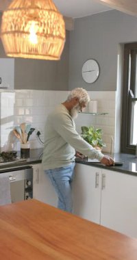 Dikey video: kıdemli Afrikalı Amerikalı adam telefonu kaldırıyor ve dizüstü bilgisayarda yazı yazıyor. Teknoloji, çalışma alanı, ev ofisi, rahat, modern, konsantrasyon, dikey video