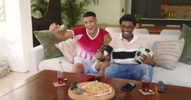 Kanepede maç izleyen çeşitli erkek arkadaşlar top ve pizzayla golü kutluyorlar. Kutlama, yoldaşlık, rahatlık, günlük, evcil, dostluk, coşku