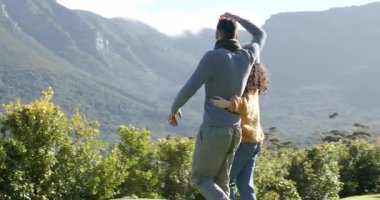 Bir çift terasta çim üzerinden dağ manzarasına doğru koşuyor, kucaklaşıp öpüşüyorlar. Macera, bağlantı, açık hava, manzara, doğa, mutluluk, keşif