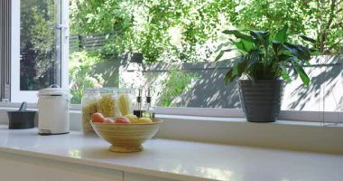 Mutfakta dolaşırken meyve kasesi, makarna kavanozları, musluk, fritöz ve saat tasarımı. Modern, minimalist, canlı, yerli, yaşam tarzı, iç mekan, rahat