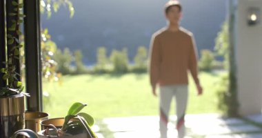 Güneş ışığı, Asyalı bir adamın elinde saksı saksısı olan verandanın sürgülü kapısından içeri girmesini sağlıyor. Sağlık, açık hava, sükunet, farkındalık, doğa, zindelik, dinginlik.