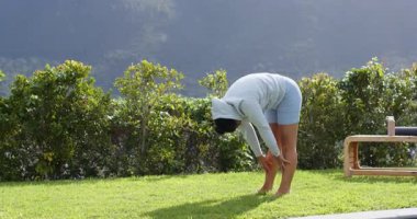 Kalçalarını esnetmeye çalışan bir kadın, Warrior II 'ye doğru atlıyor, havuz kenarındaki çimlere yan açıyla süpürüyor. Spor, sağlık, açık hava, huzur, farkındalık, egzersiz, doğal