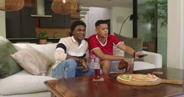 Farklı erkek arkadaşlar televizyondaki hedefe uzaktan kumandalı koltuktan tepki veriyor, pizzanın yanında yumruk sallıyorlar. Gündelik, eğlence, rahatlama, sosyalleşme, modern, canlı, boş zaman